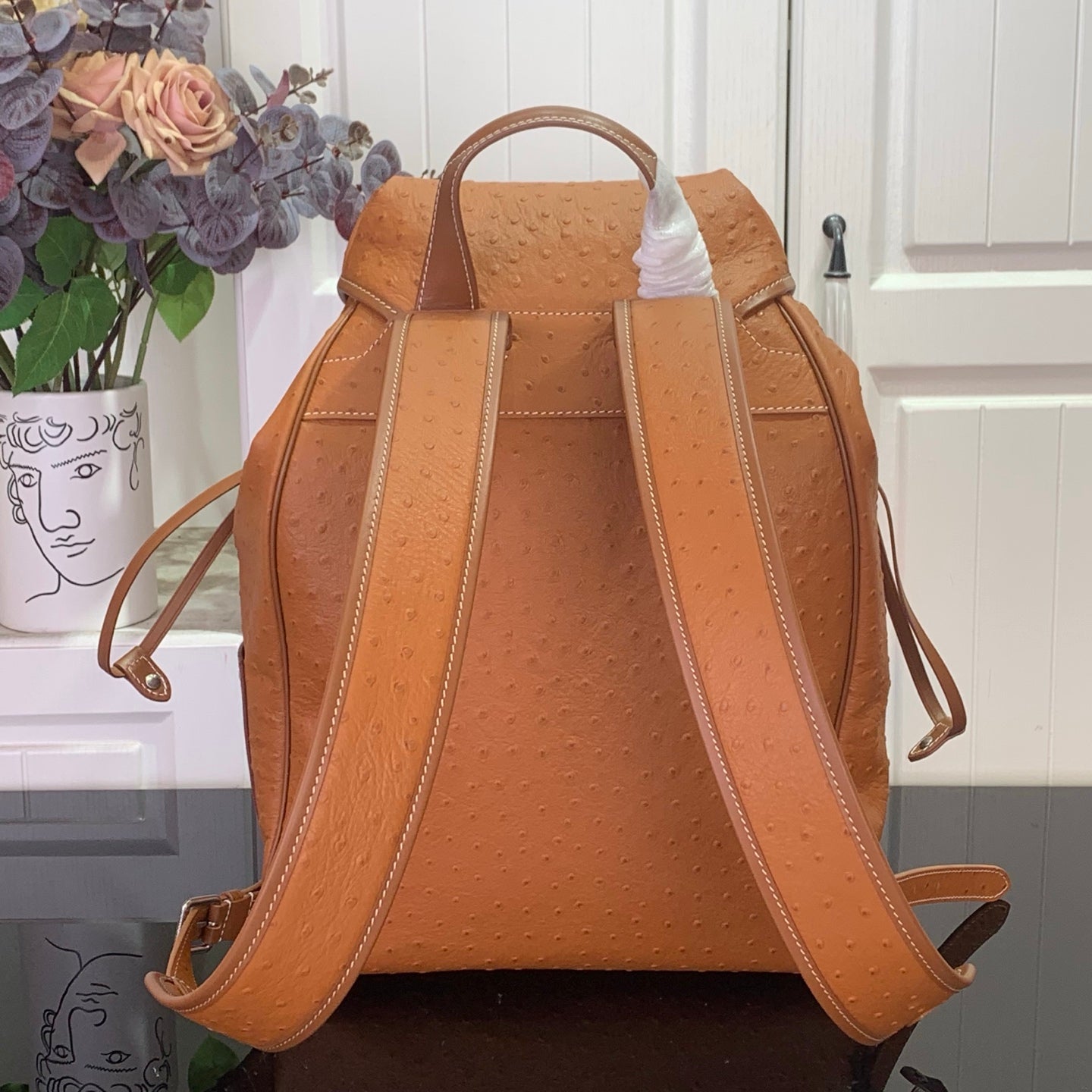 Cognac brown leather backpack with wide adjustable shoulder straps and top handle.