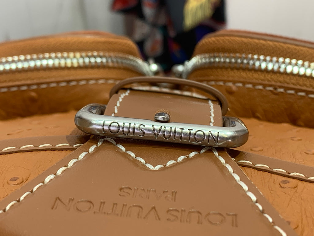 Leather flap hardware with metal ring stamped 'LOUIS VUITTON' and stitched edge.
