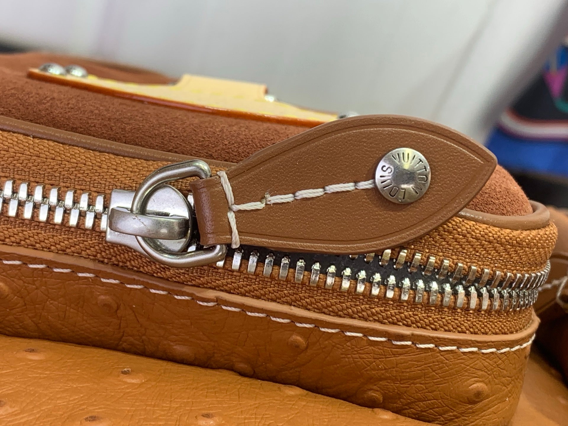 Leather bag zipper pull with metal ring and stitching on cognac strap.