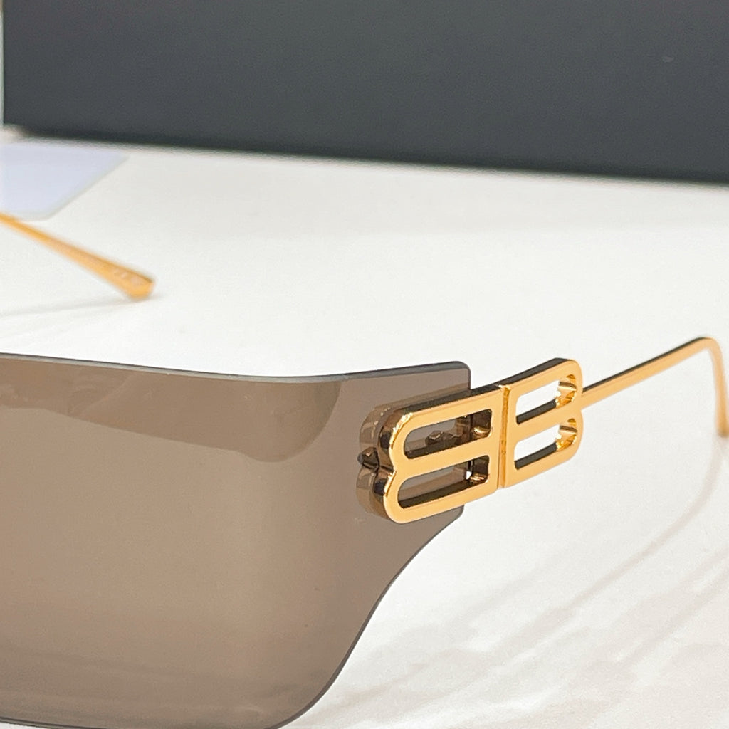 Sunglasses temple close-up with gold-tone geometric logo and translucent lens edge.