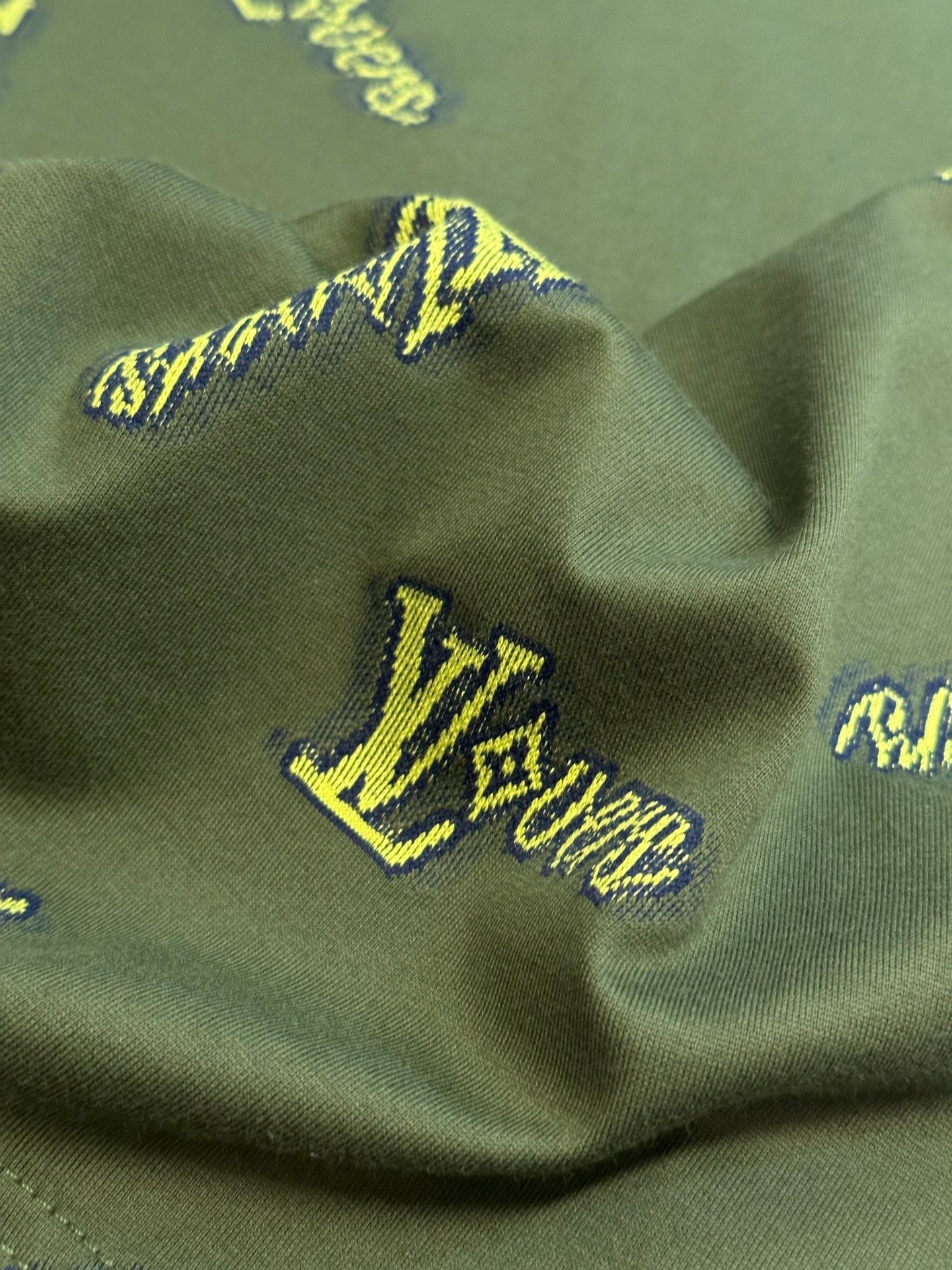 Green shirt with yellow LV-style logo embroidery on textured fabric