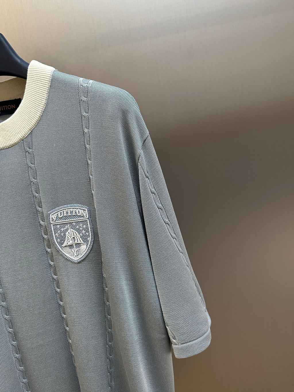 Close-up of light blue knit polo with chest shield logo patch