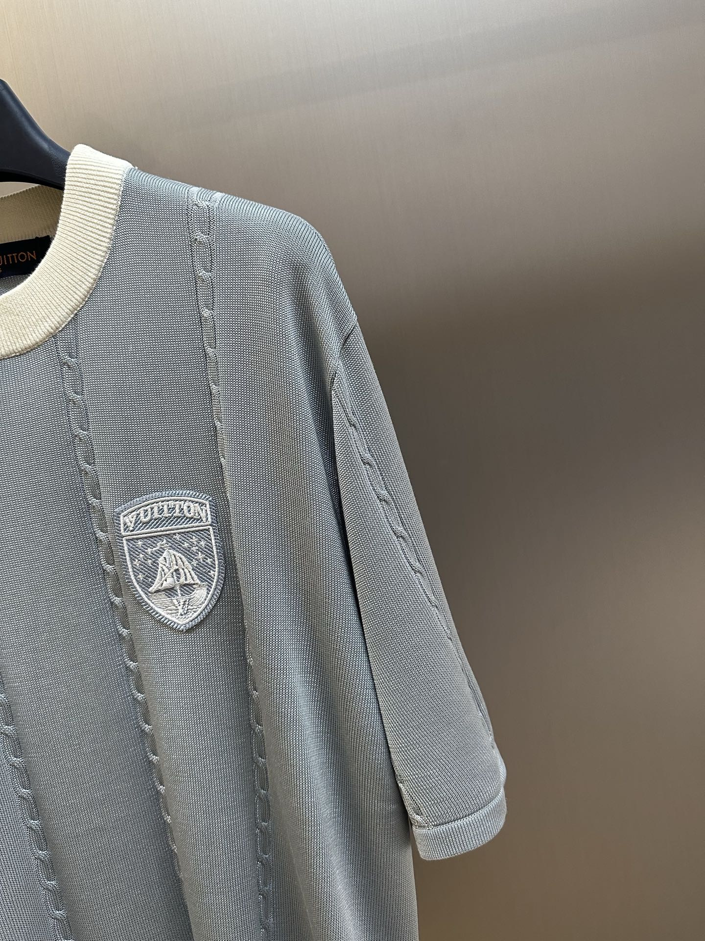Close-up of light blue knit polo with chest shield logo patch