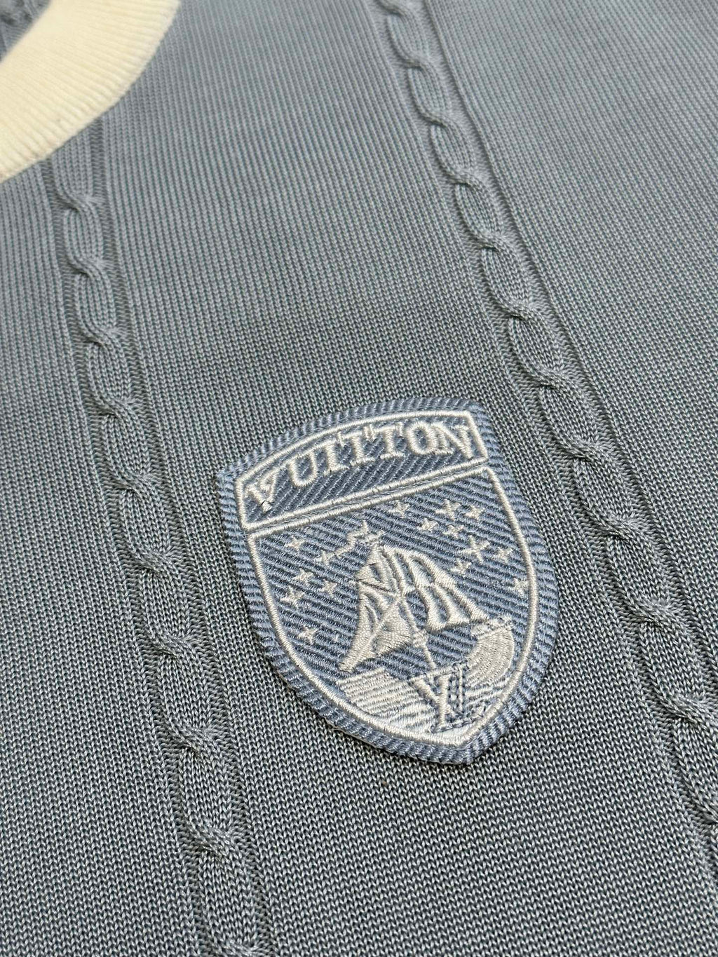 Close-up of Louis Vuitton shield logo badge on light blue knit polo