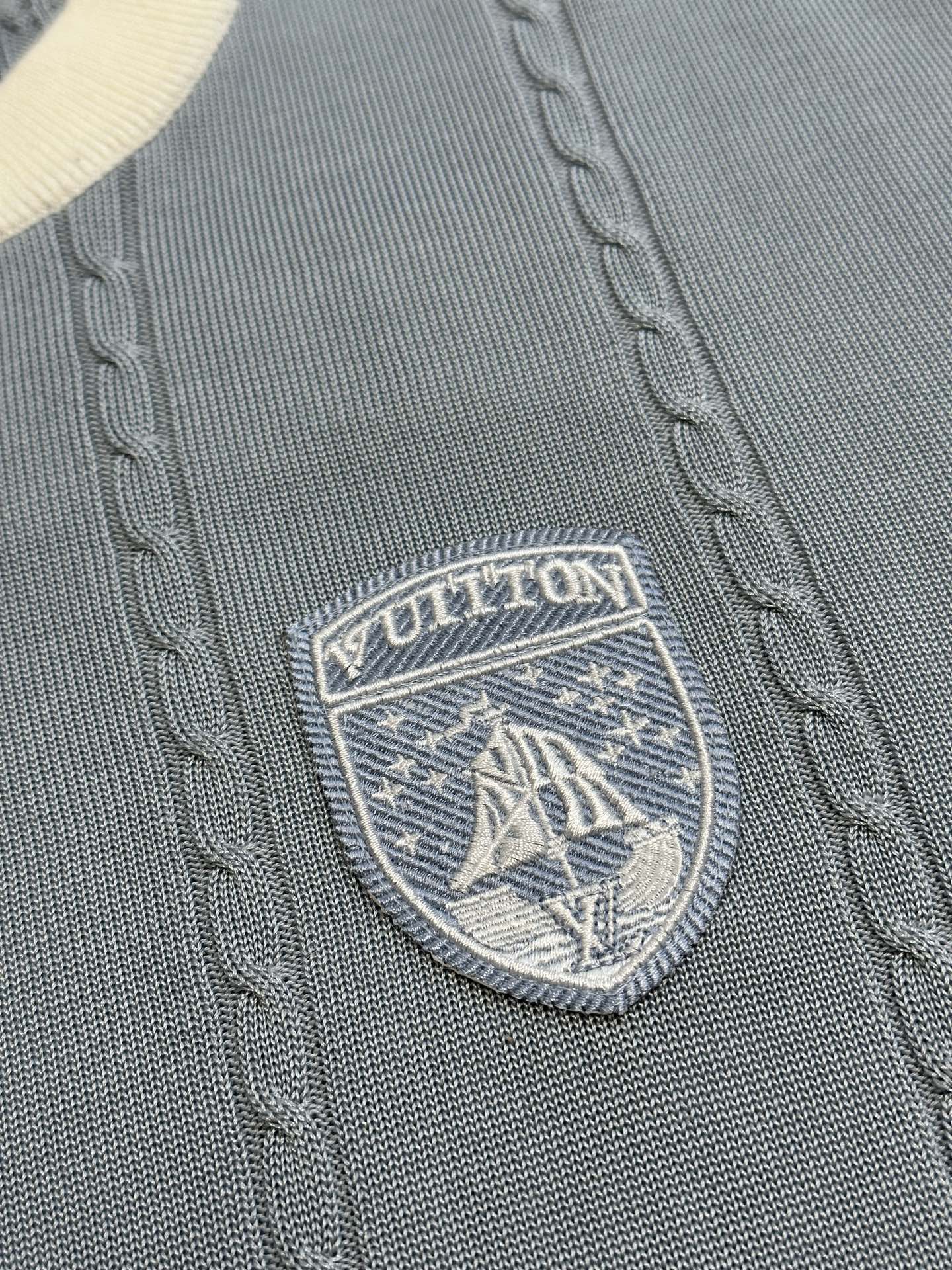 Close-up of Louis Vuitton shield logo badge on light blue knit polo