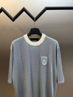 Light blue knit polo shirt with shield logo patch on chest