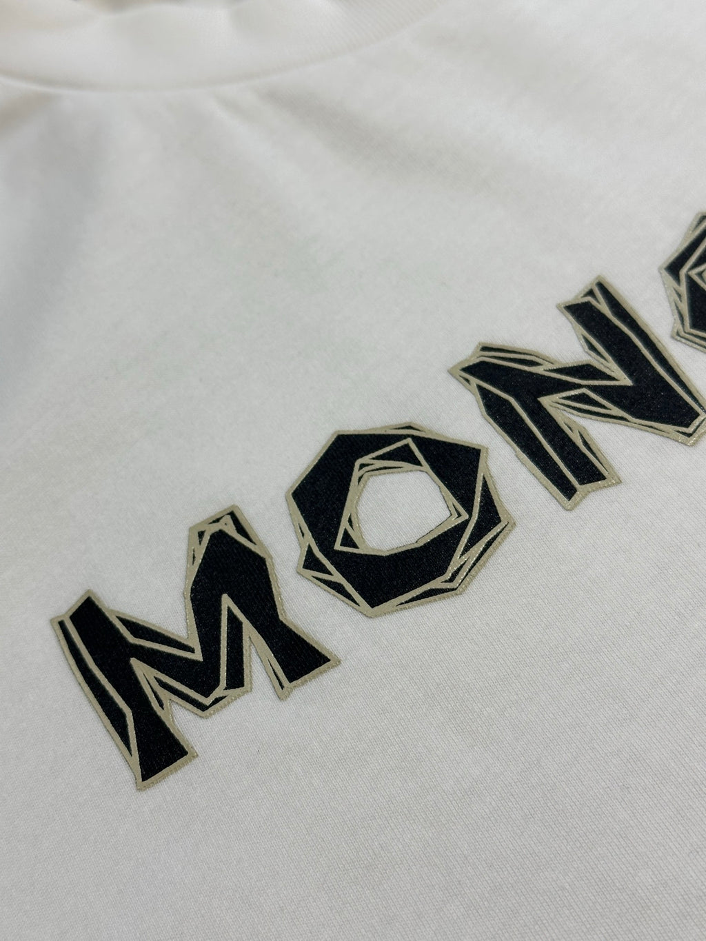 White Moncler T-shirt with large black logo wordmark across chest.