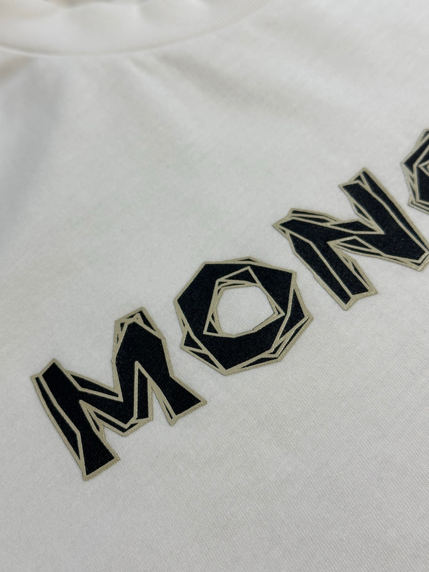 White Moncler T-shirt with large black logo wordmark across chest.