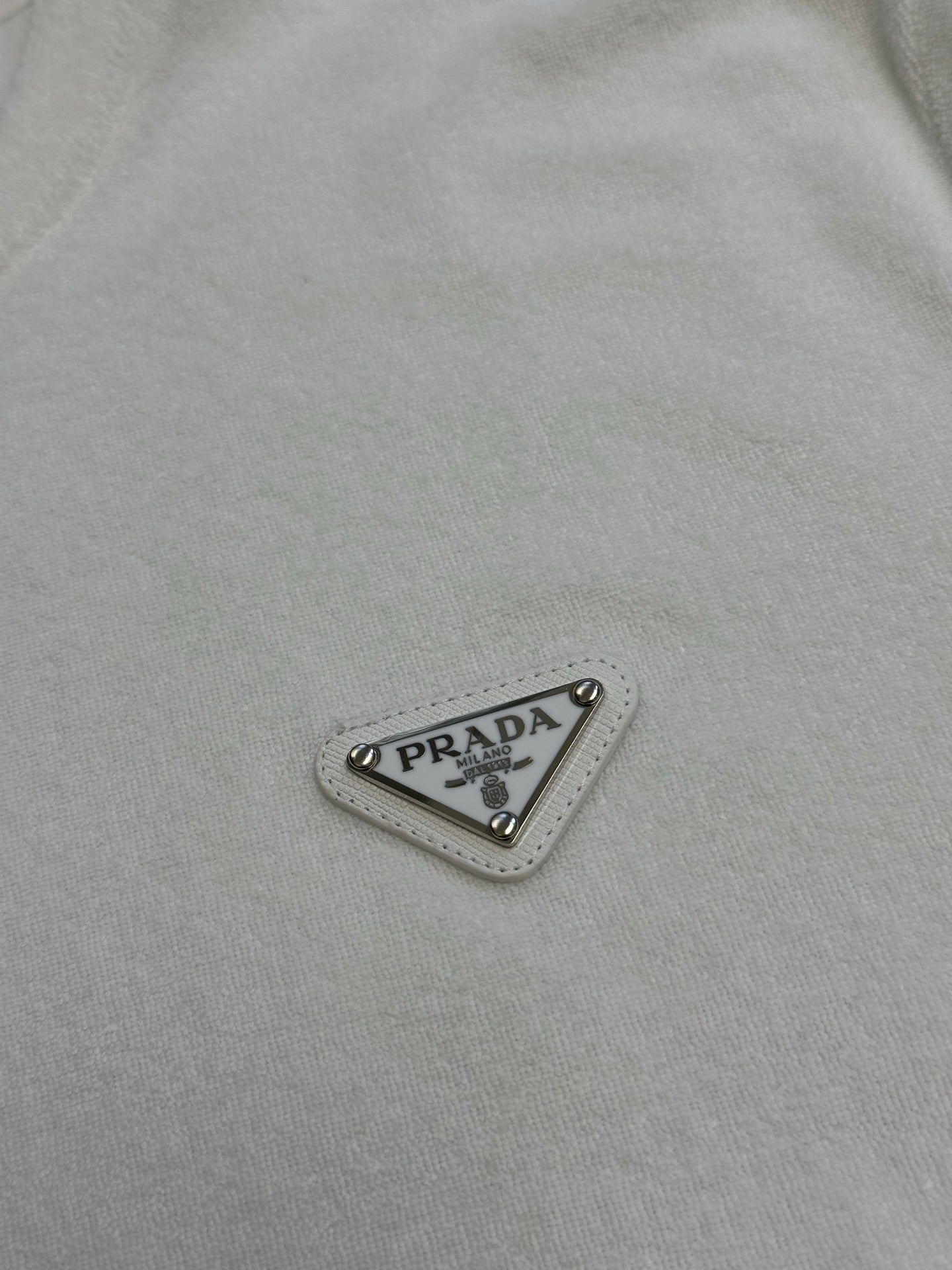Prada triangular logo patch with “PRADA” text on white T-shirt fabric