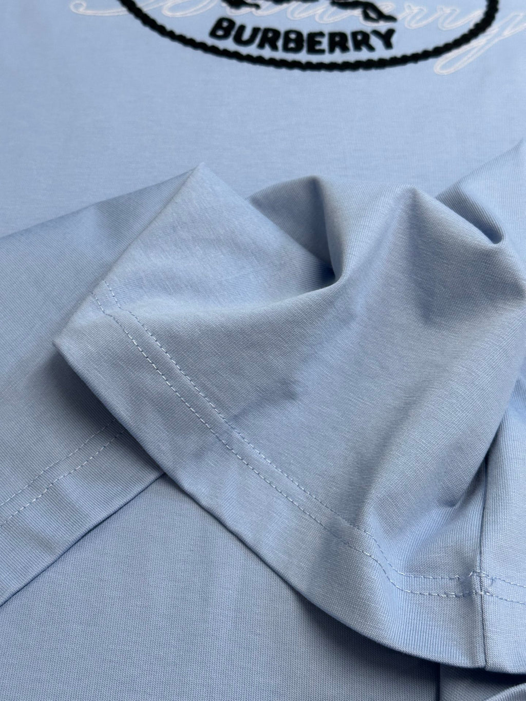 Light blue Burberry T-shirt fabric close-up with stitched hem and collar