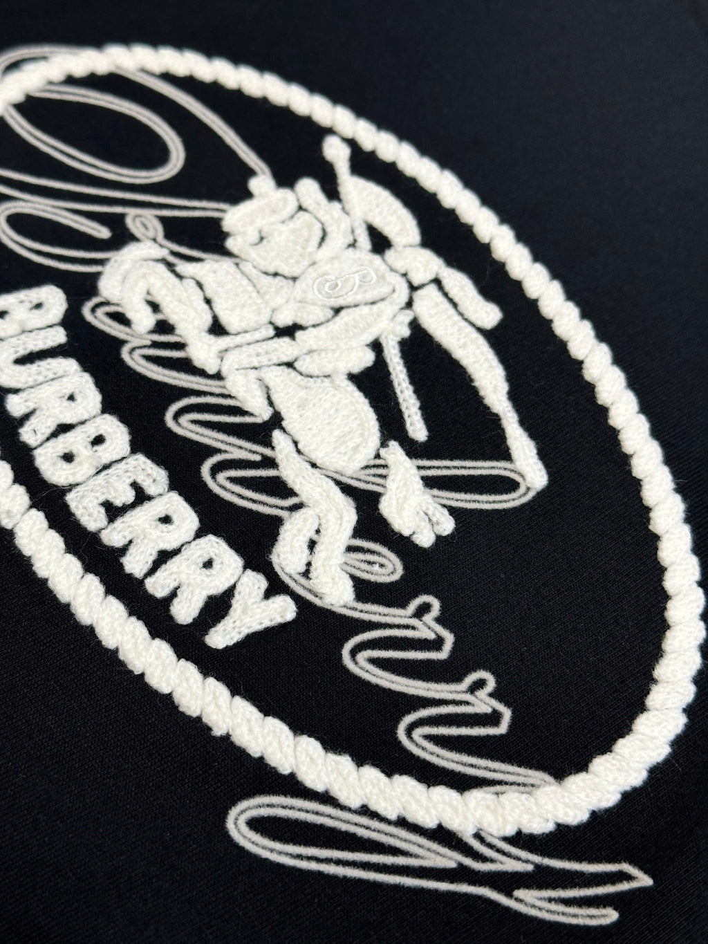 Close-up of white embroidered Burberry oval logo on black T-shirt
