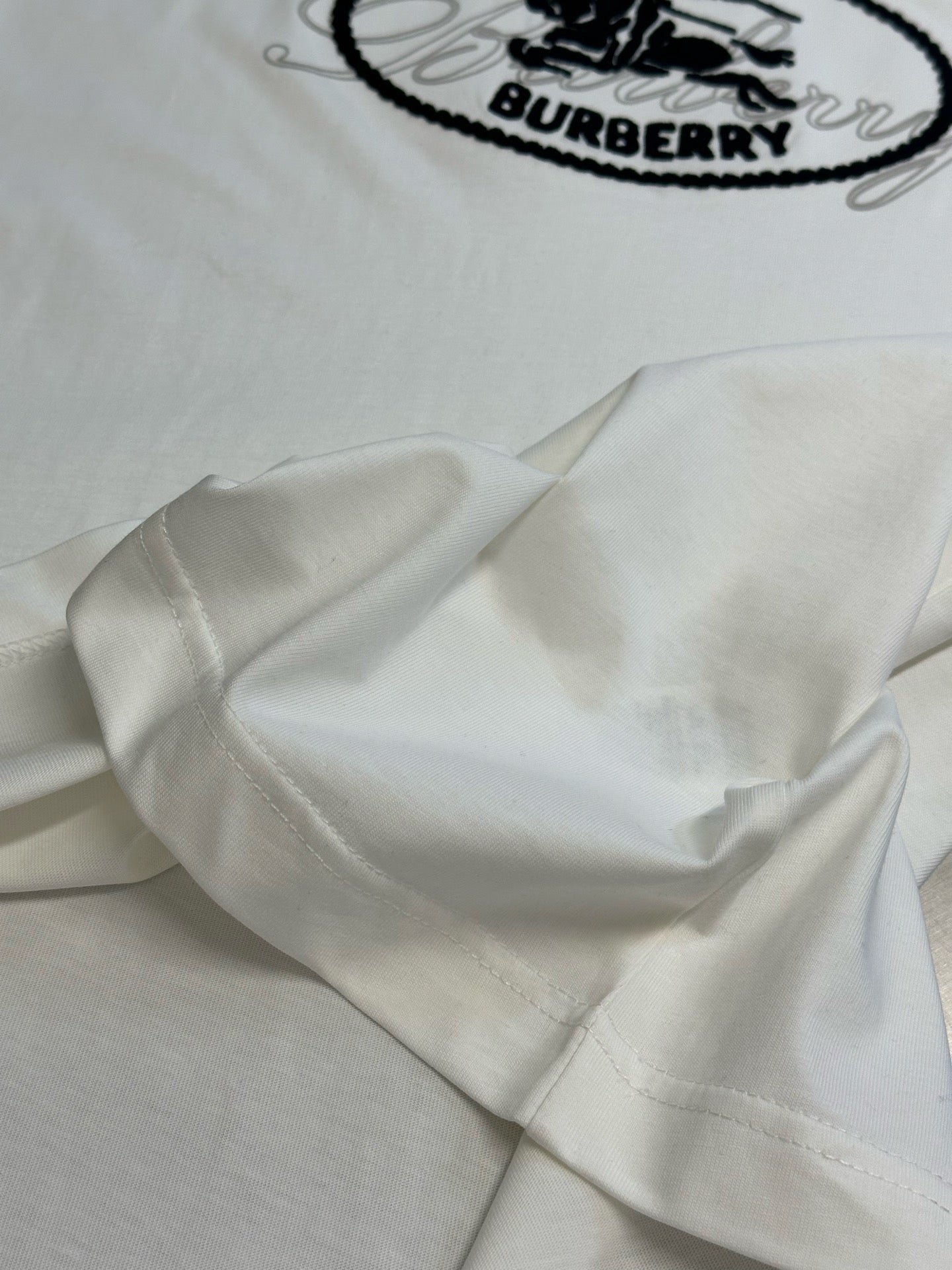 White T-shirt sleeve close-up with part of the black oval Burberry logo