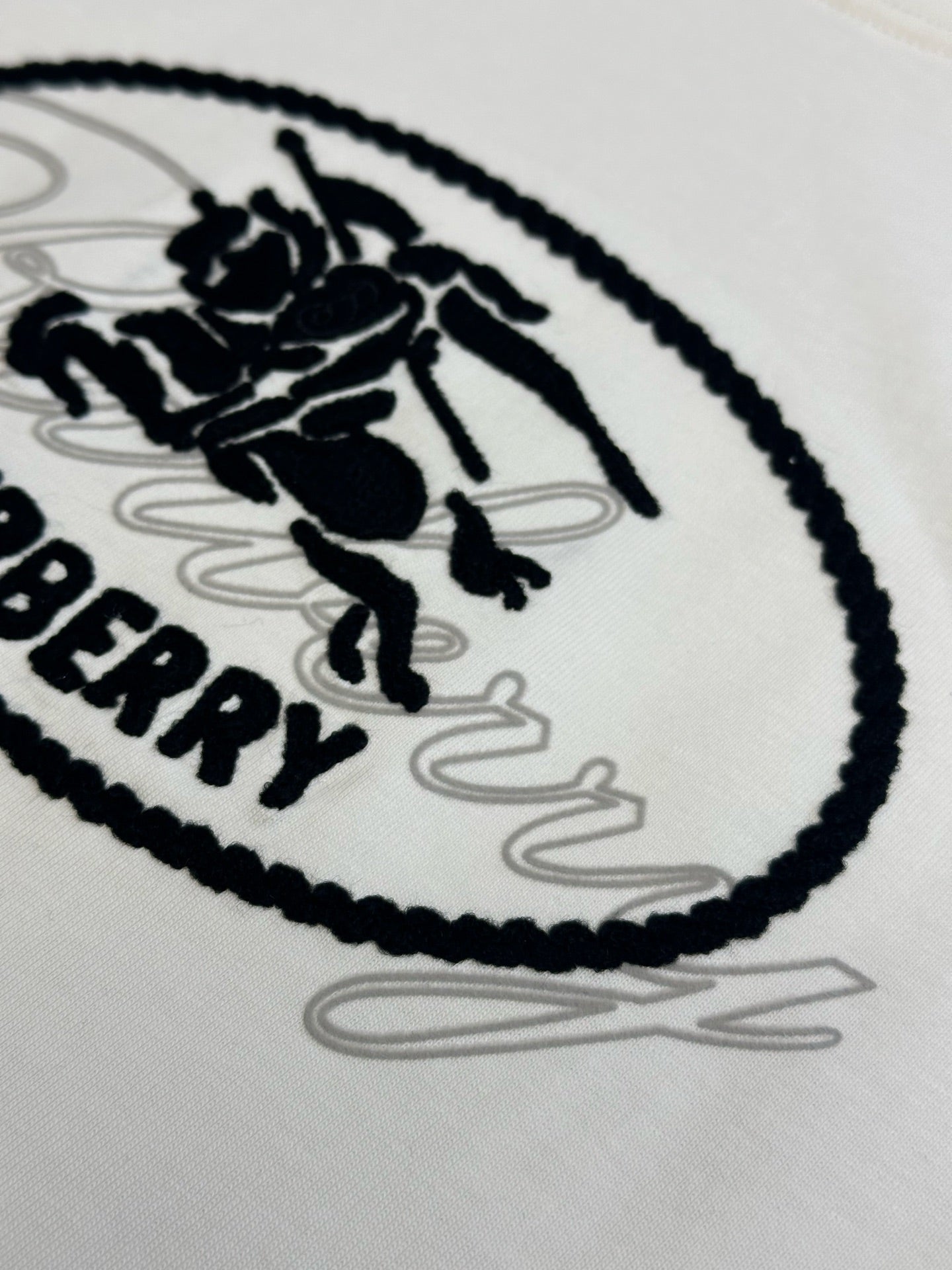 White Burberry oval logo T-shirt close-up, black stitched edging and sketch lines