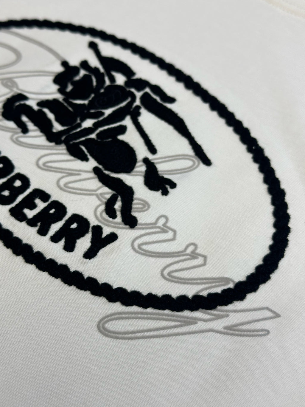 Close-up of black oval Burberry logo graphic on a white T-shirt