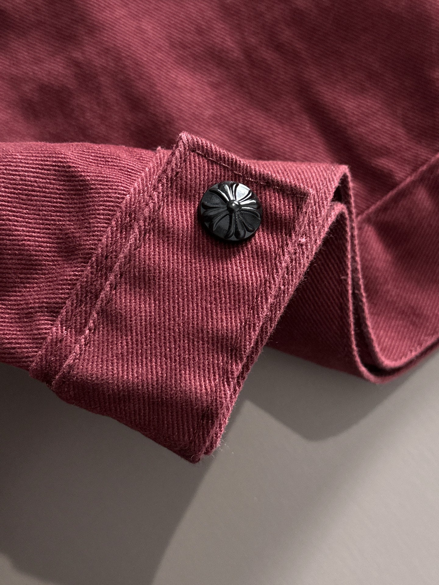 Maroon denim jacket sleeve with dark decorative snap and folded cuff detail