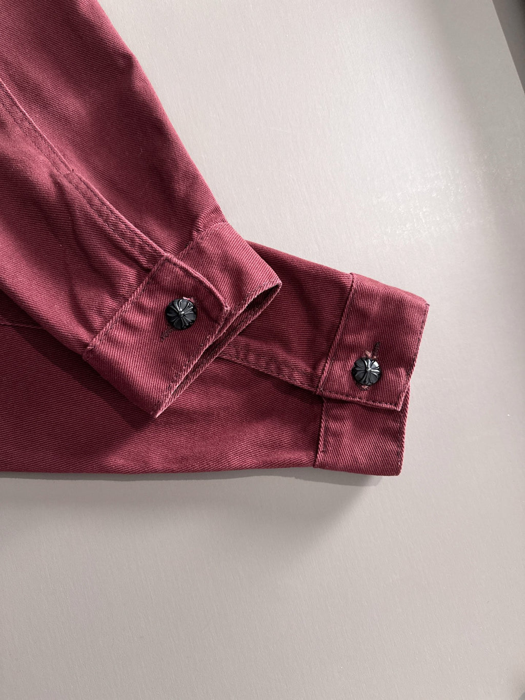 Maroon denim jacket sleeve cuff with dark snap buttons and stitched details