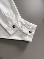 White denim jacket cuff with black decorative snap buttons and stitched detail