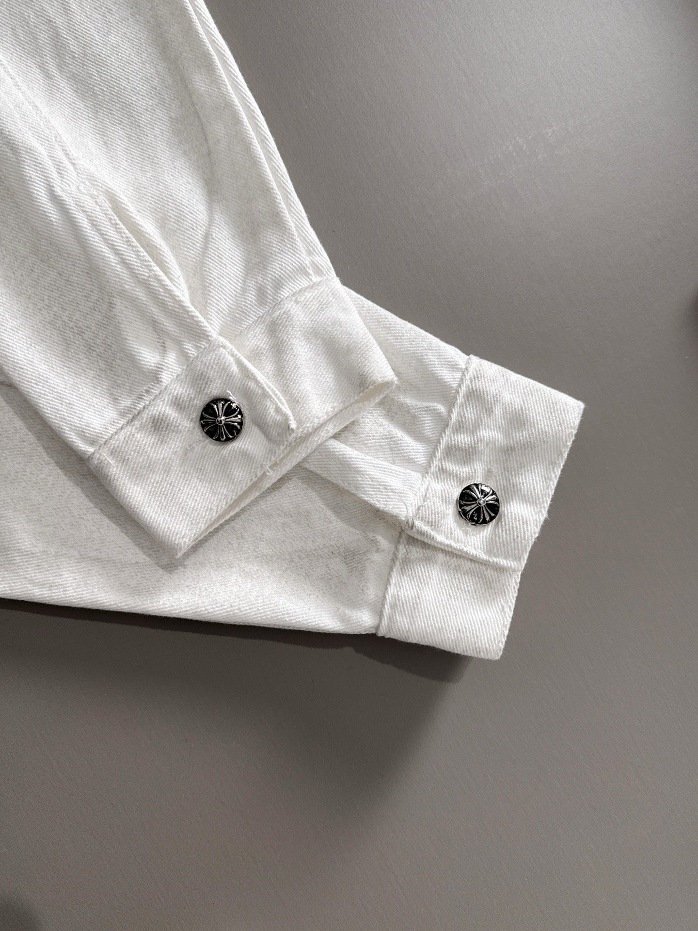 White denim jacket cuff with black decorative snap buttons and stitched detail