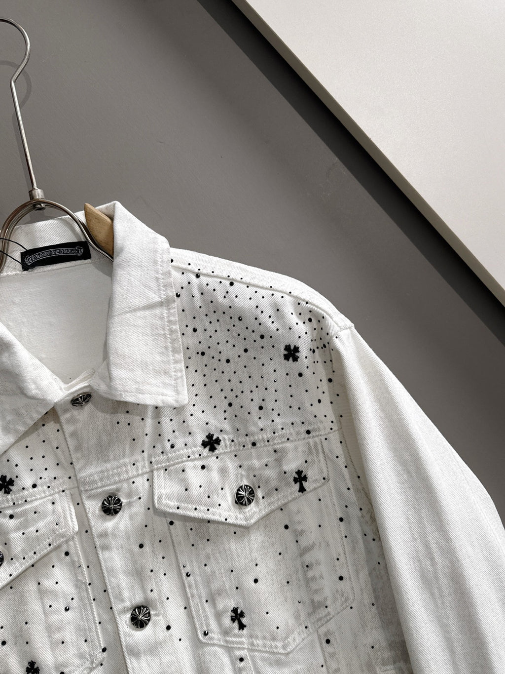 White denim jacket detail with black dot pattern and star patches, buttoned chest pockets