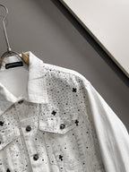 White denim jacket detail with black dot pattern and star patches, buttoned chest pockets
