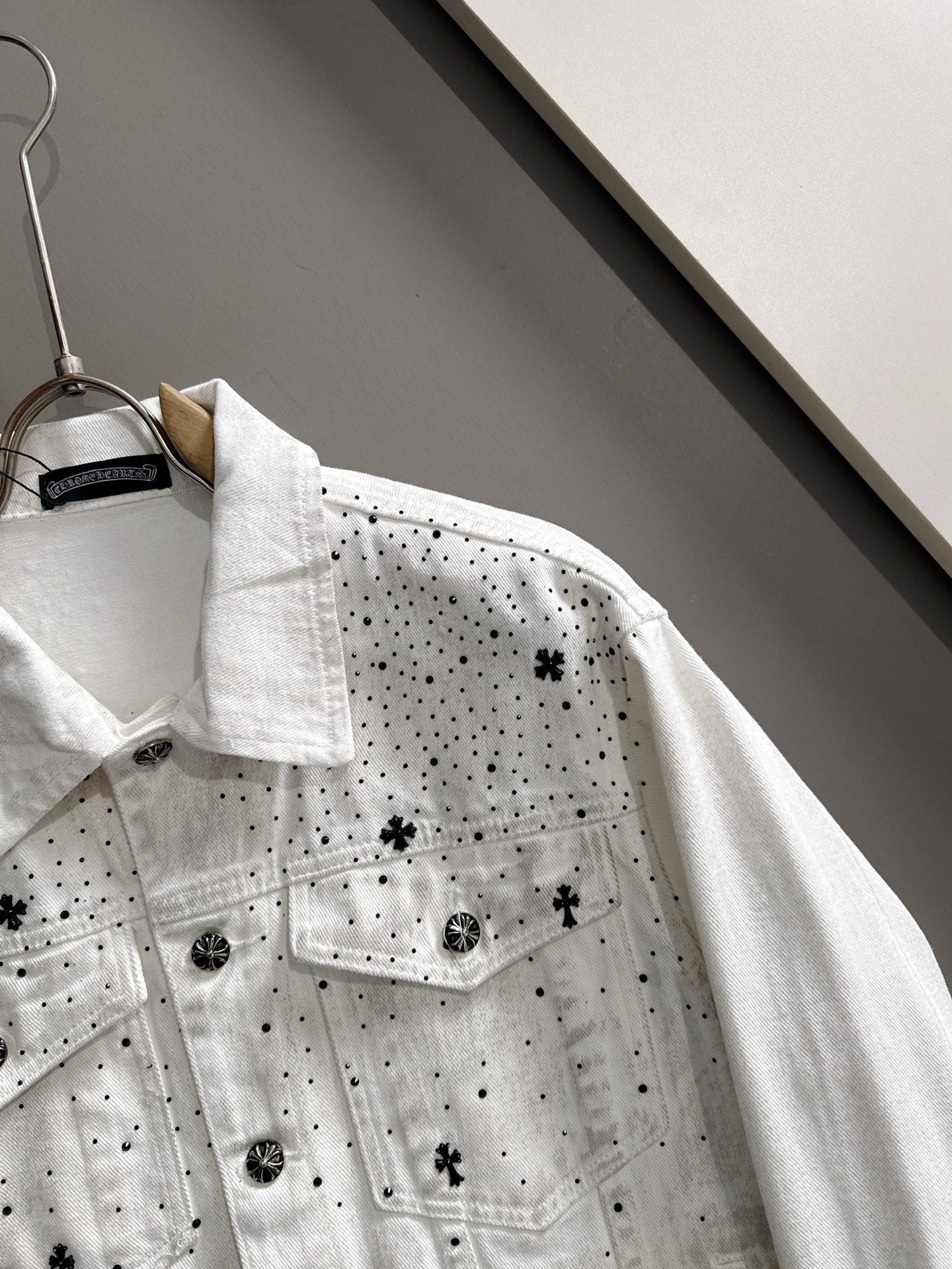White denim jacket detail with black dot pattern and star patches, buttoned chest pockets