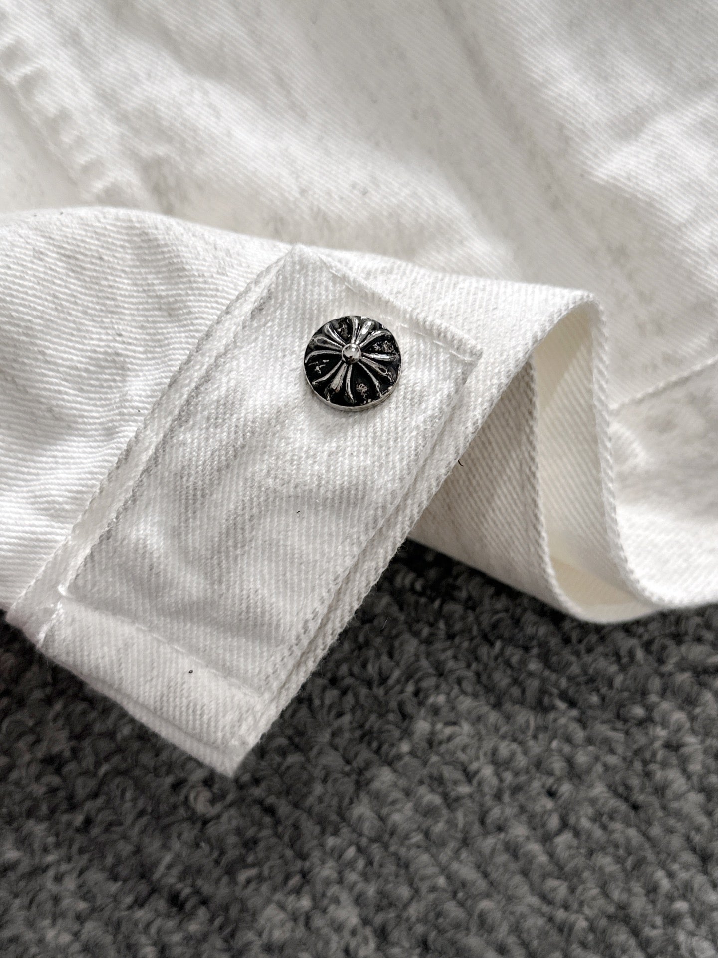 White denim jacket sleeve cuff with black decorative button and folded hem