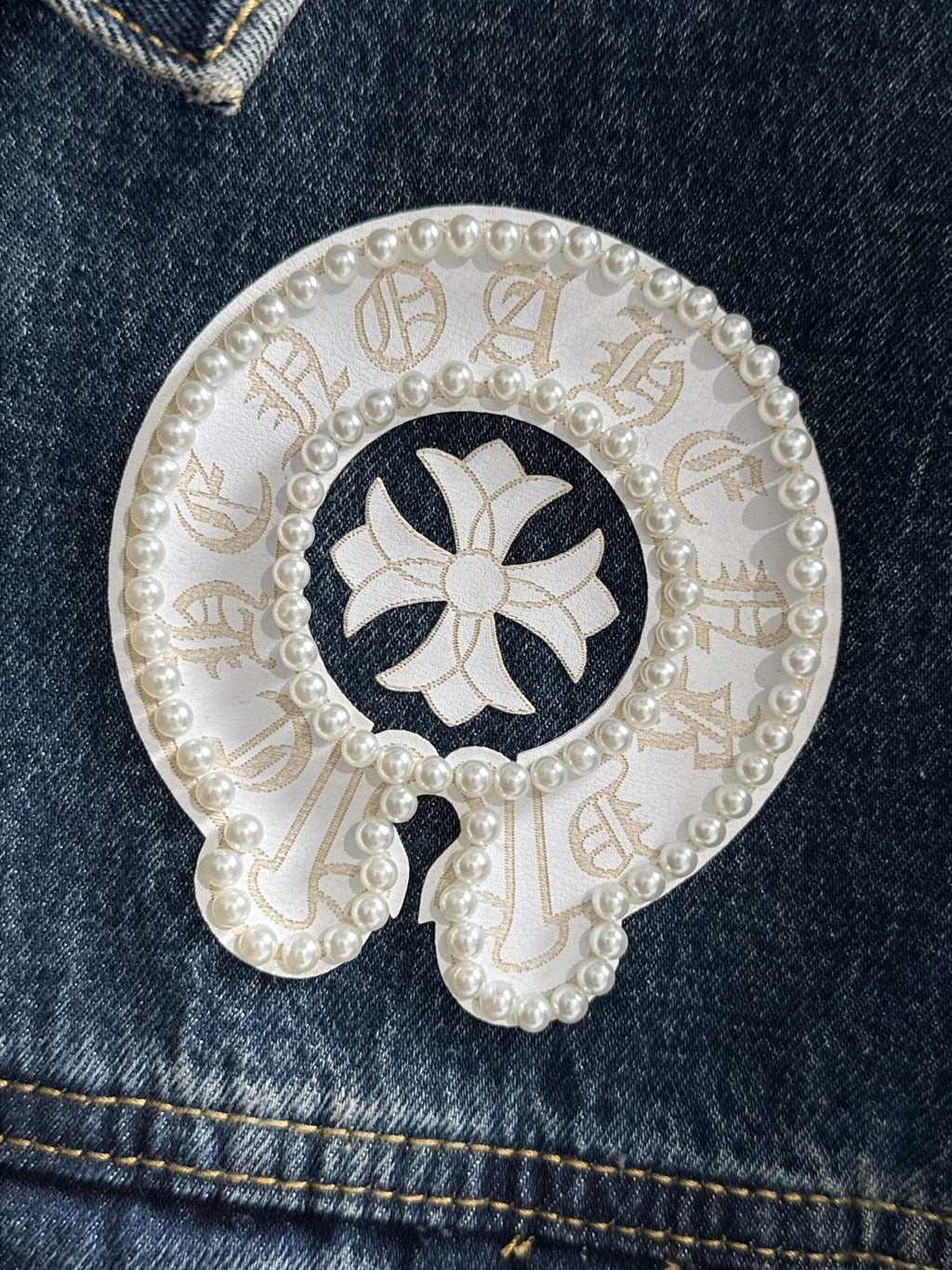Circular white pearl patch on dark denim with dark flower-like emblem