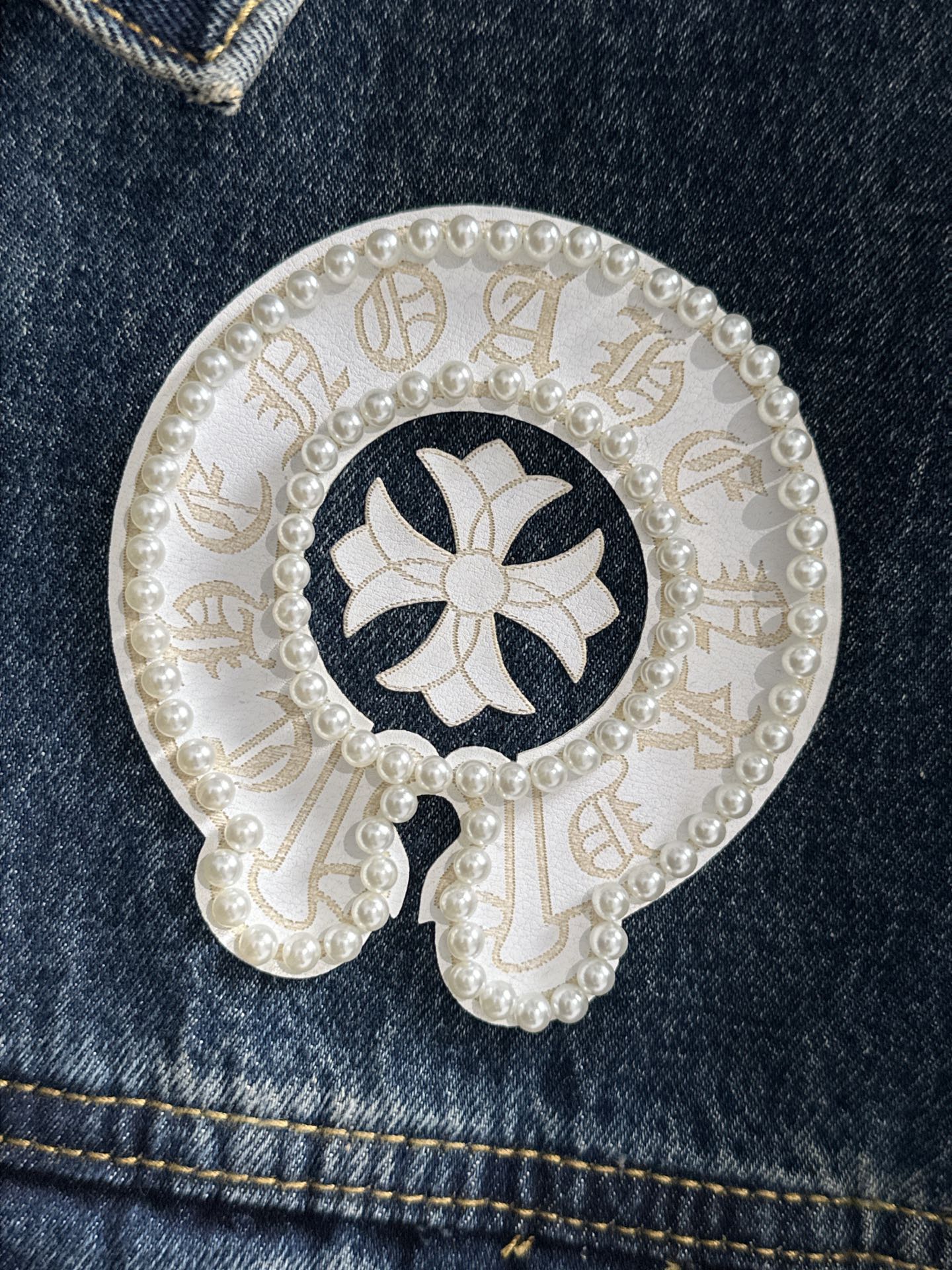 Circular white pearl patch on dark denim with dark flower-like emblem