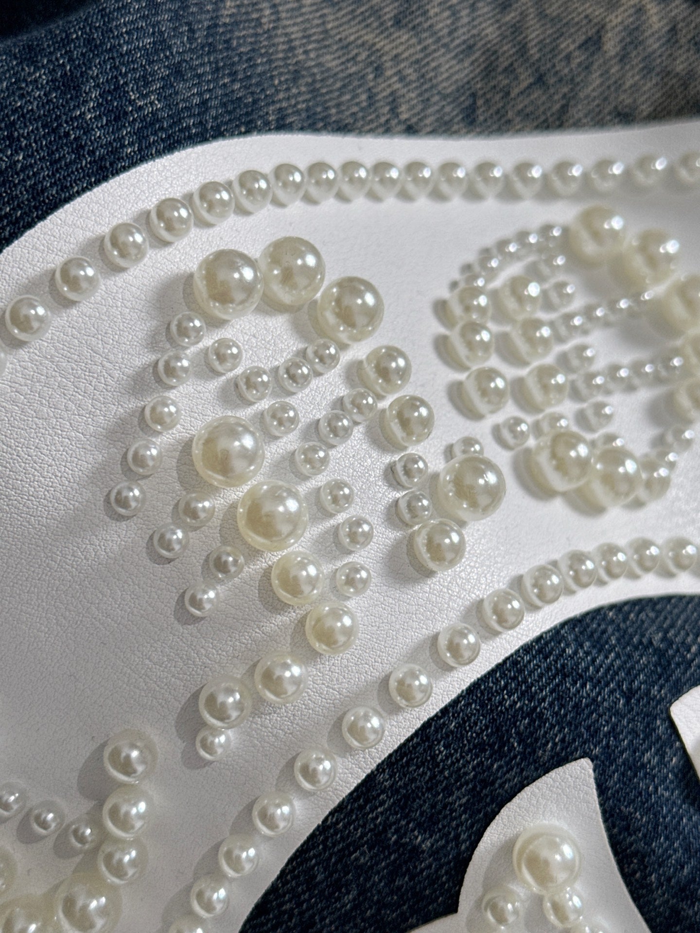 Pearl beaded detailing on white fabric patch forming a decorative letter-like design