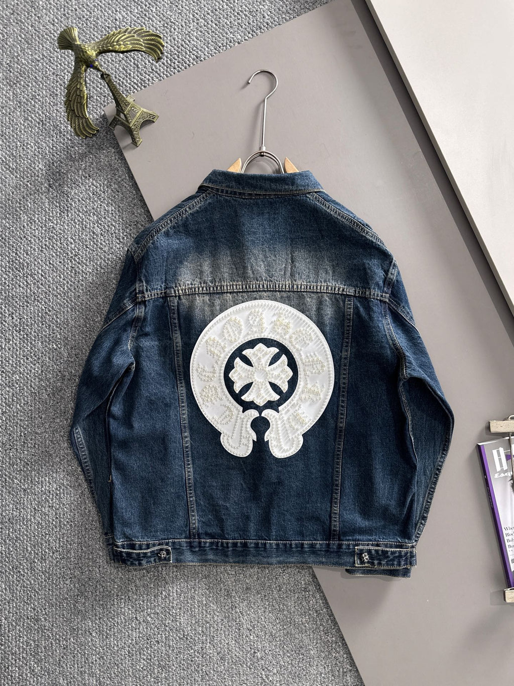 Blue long denim jacket back view with large white pearl emblem on center