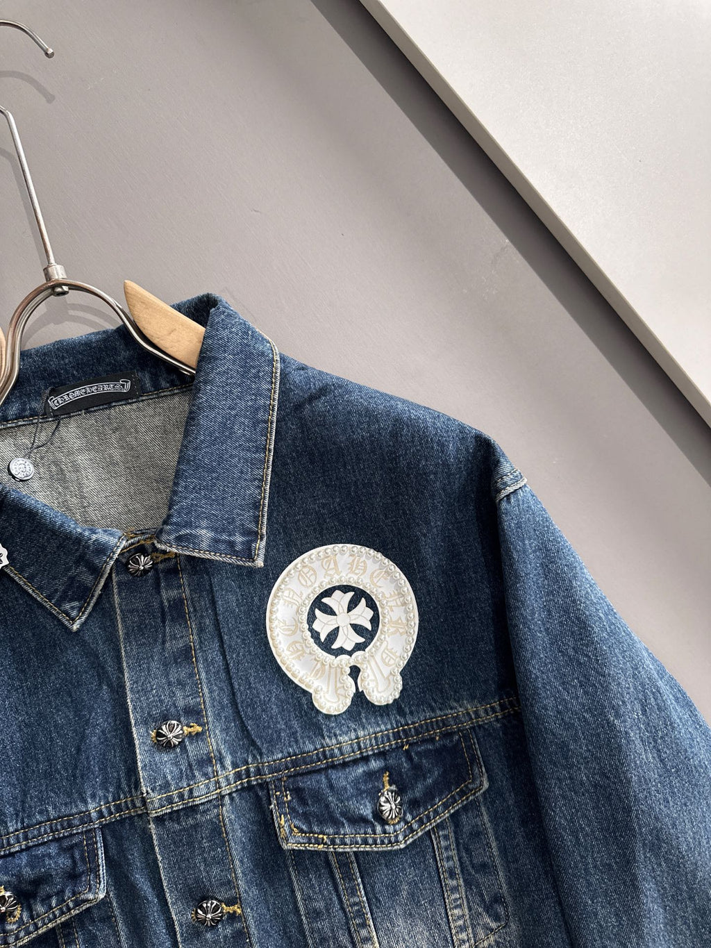 Blue denim jacket close-up with pearl-embroidered round emblem on chest pocket
