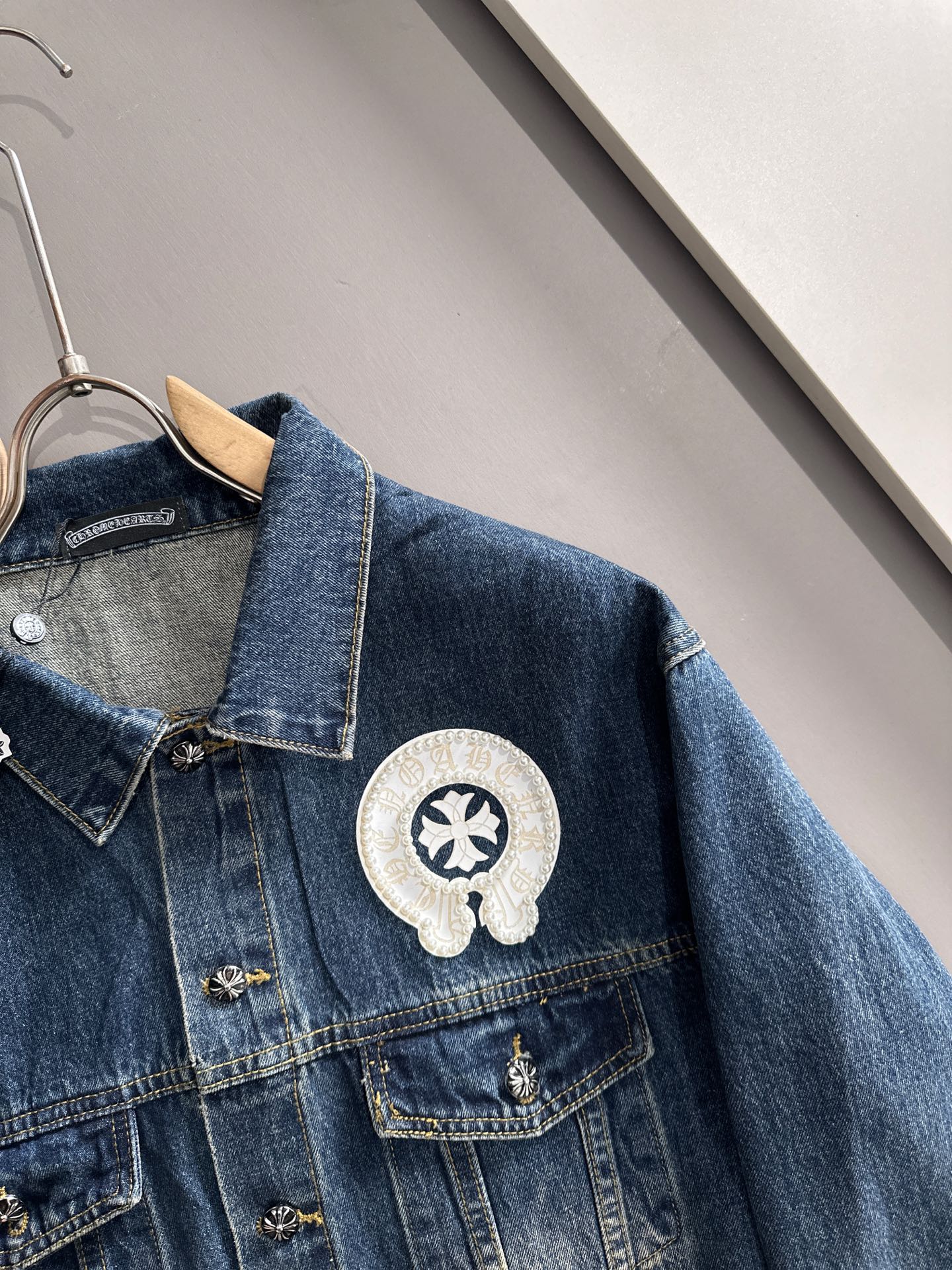 Blue denim jacket close-up with pearl-embroidered round emblem on chest pocket