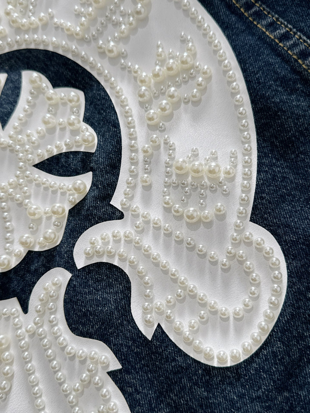 Beaded pearl embroidery filling a white decorative patch on dark denim