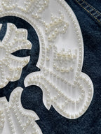Beaded pearl embroidery filling a white decorative patch on dark denim