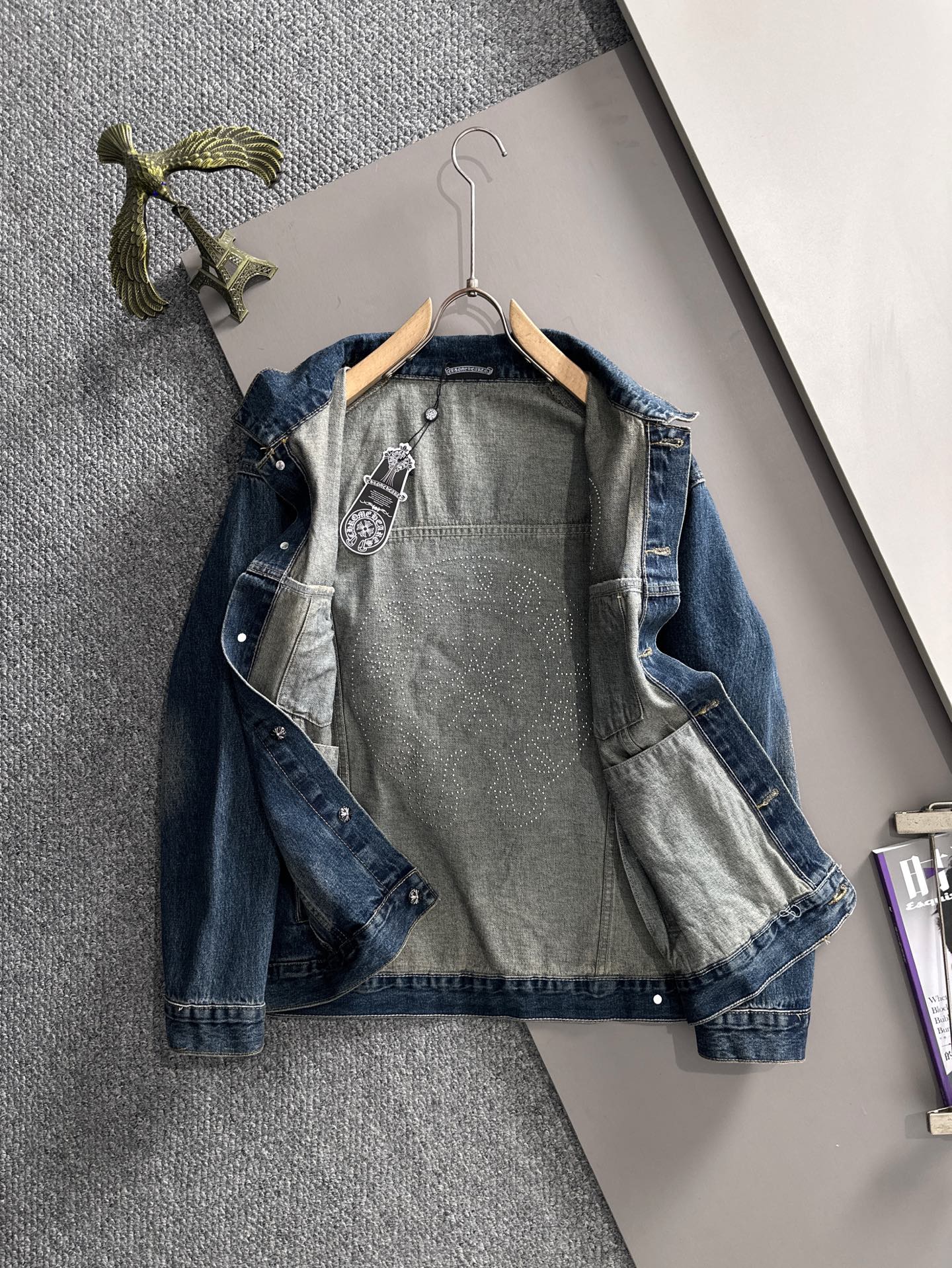 Blue long denim jacket laid flat on hanger with front graphic panels