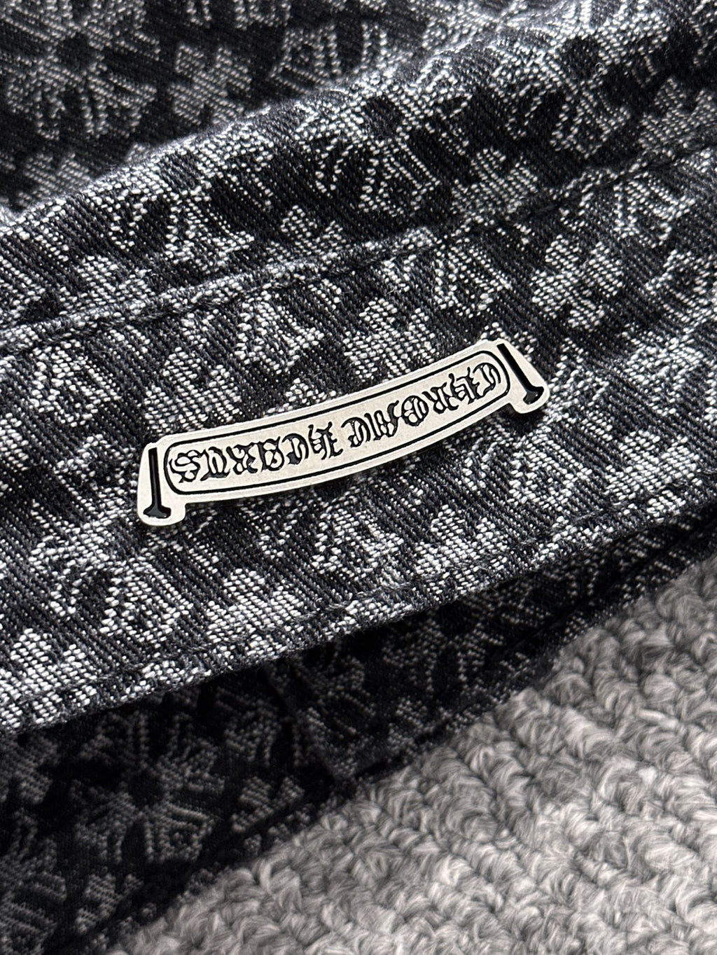 Close-up of patterned jacket fabric and metal brand-style logo patch