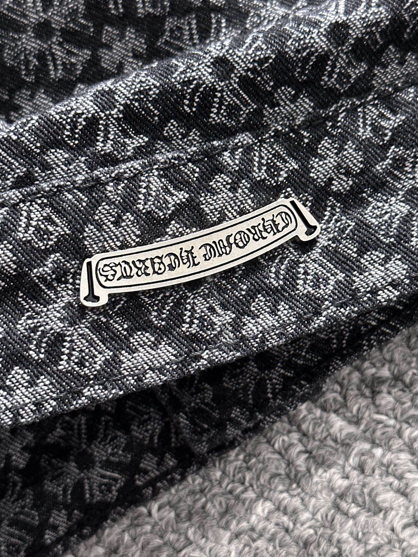 Close-up of patterned jacket fabric and metal brand-style logo patch