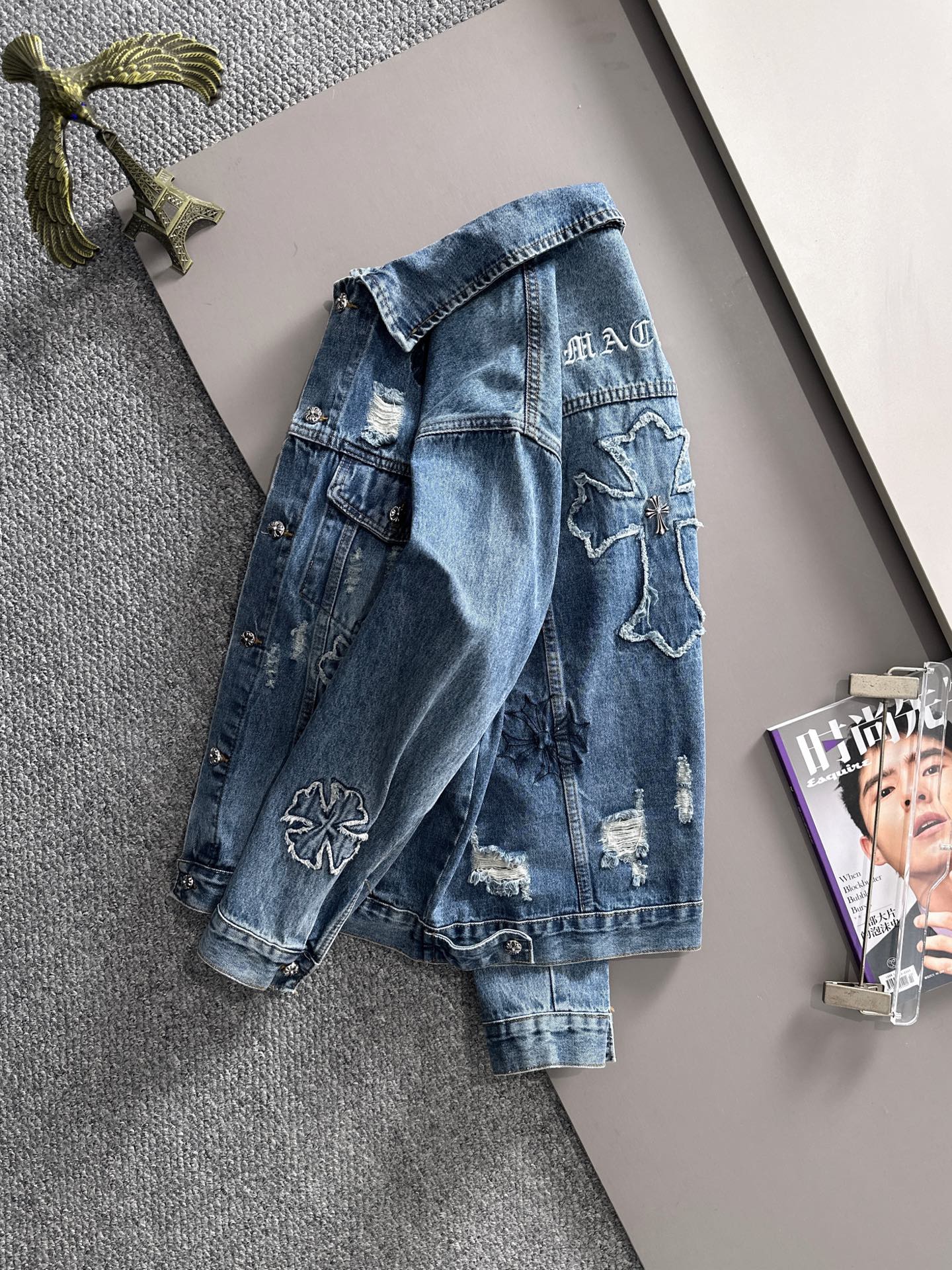 Blue denim jacket back view with embroidered cross patch and distressed finish