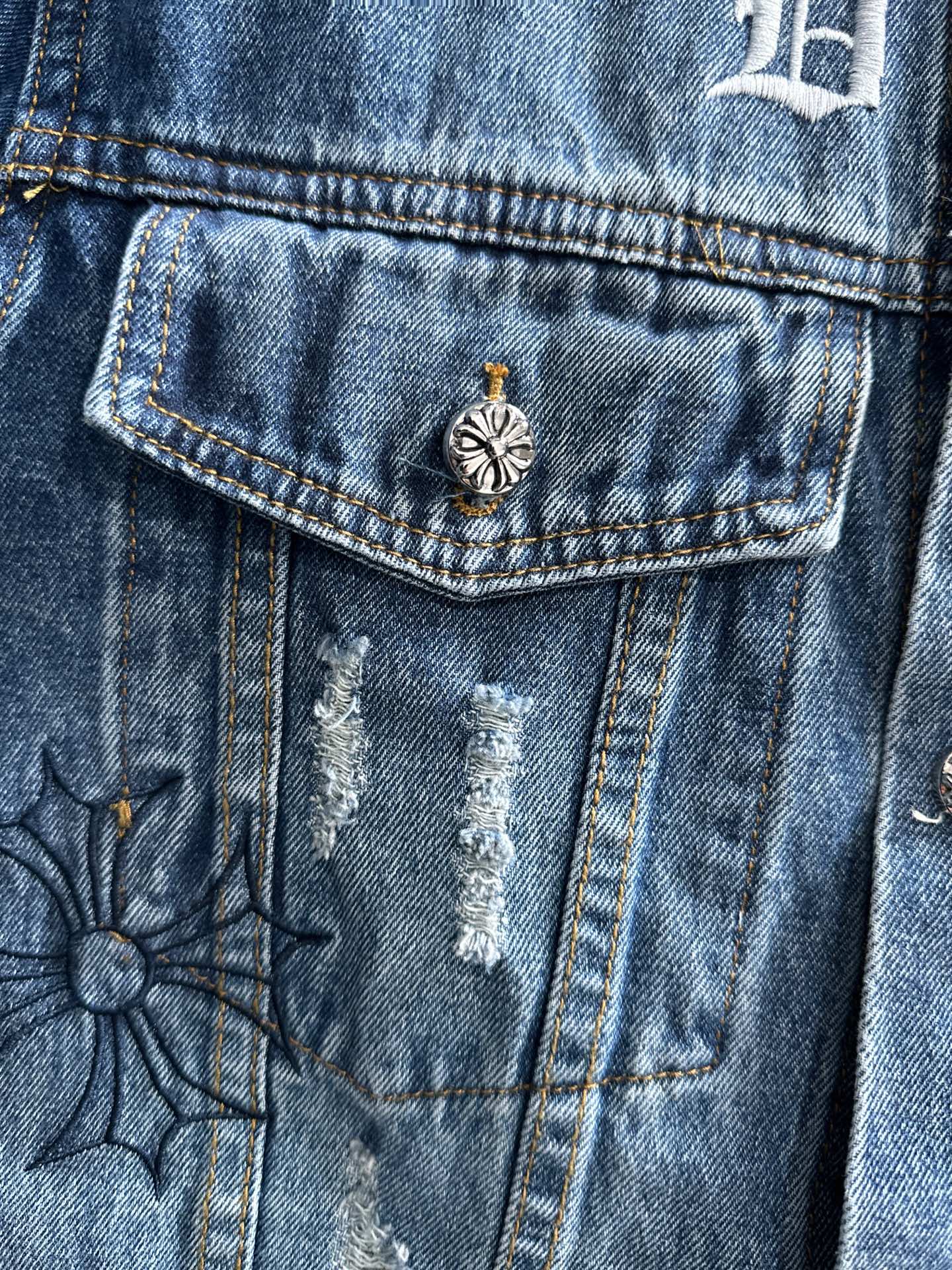 Blue denim jacket chest pocket with small flower emblem and stitched detailing