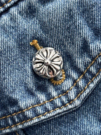 Blue denim jacket button detail with metal cross emblem and gold stitching