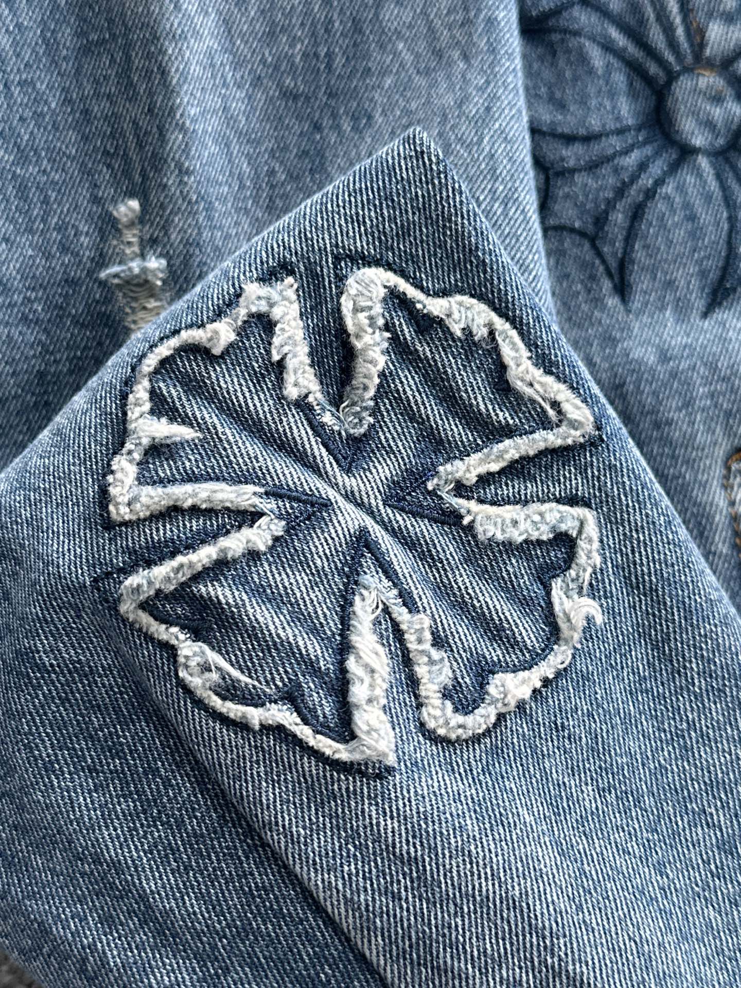 Blue denim jacket sleeve with oversized embroidered snowflake-style emblem