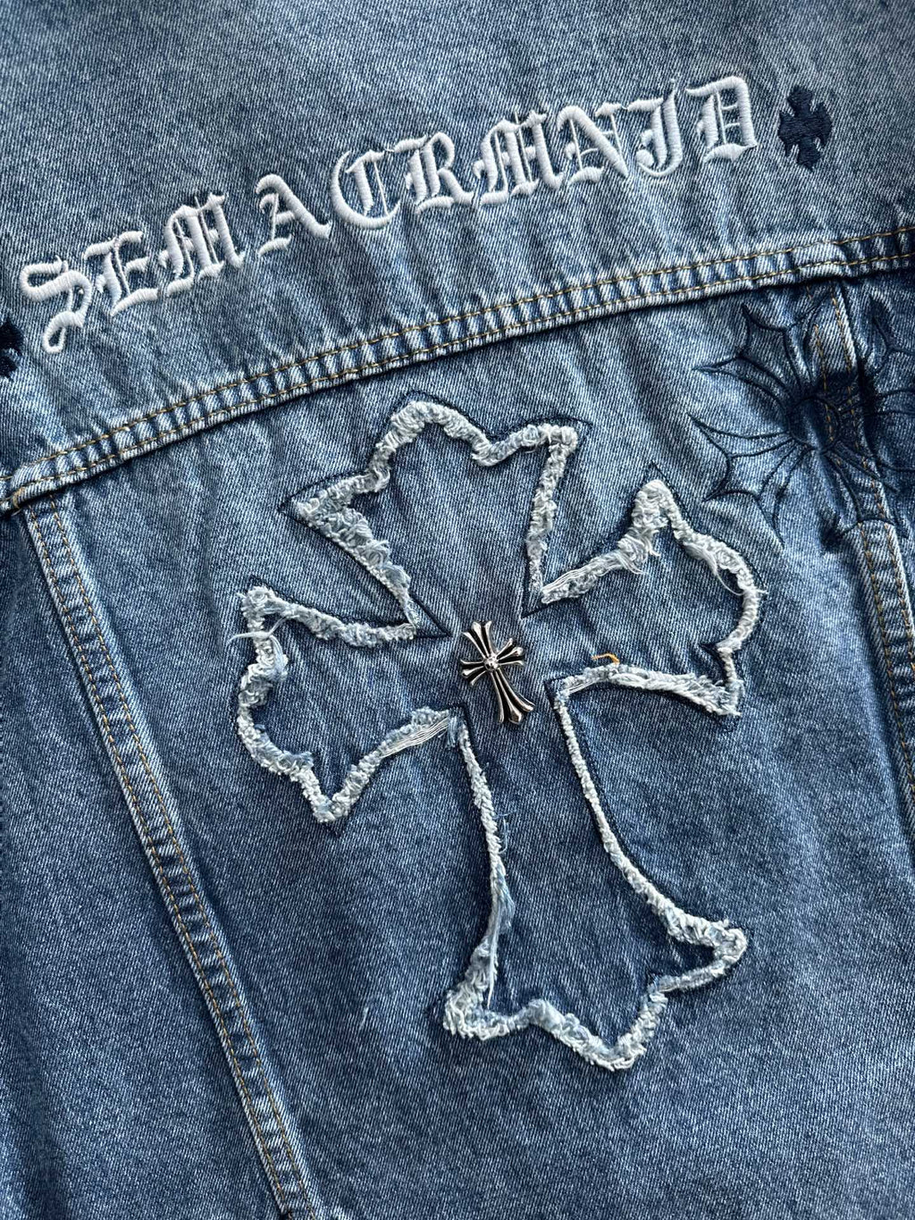 Blue denim jacket back with large cross-shaped embroidered graphic