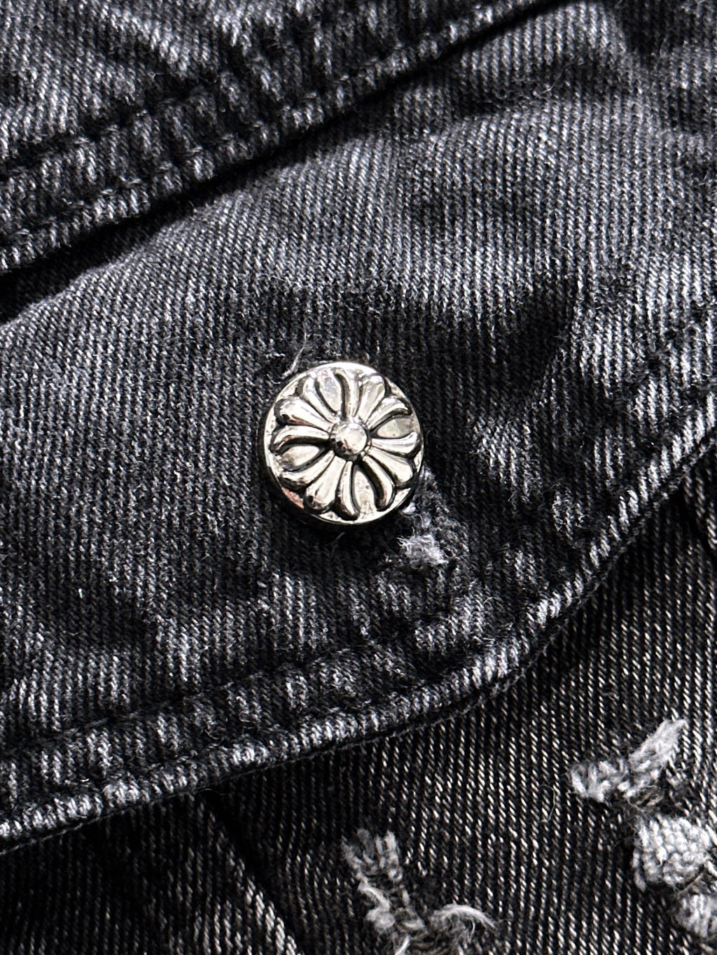 Dark denim jacket pocket flap with round metal button and embroidered details
