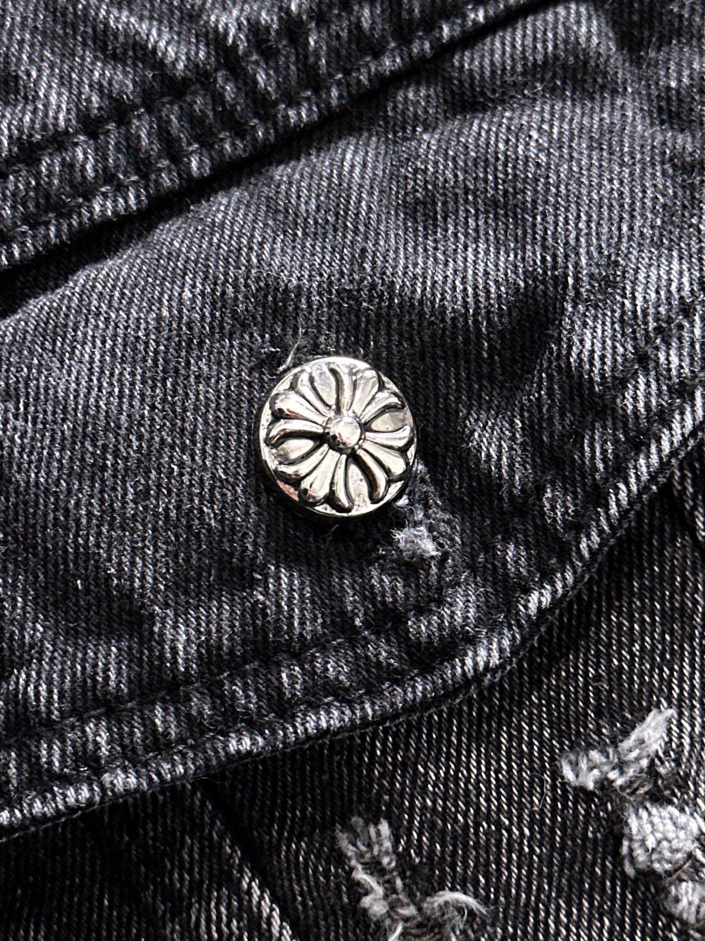 Dark denim jacket pocket flap with round metal button and embroidered details