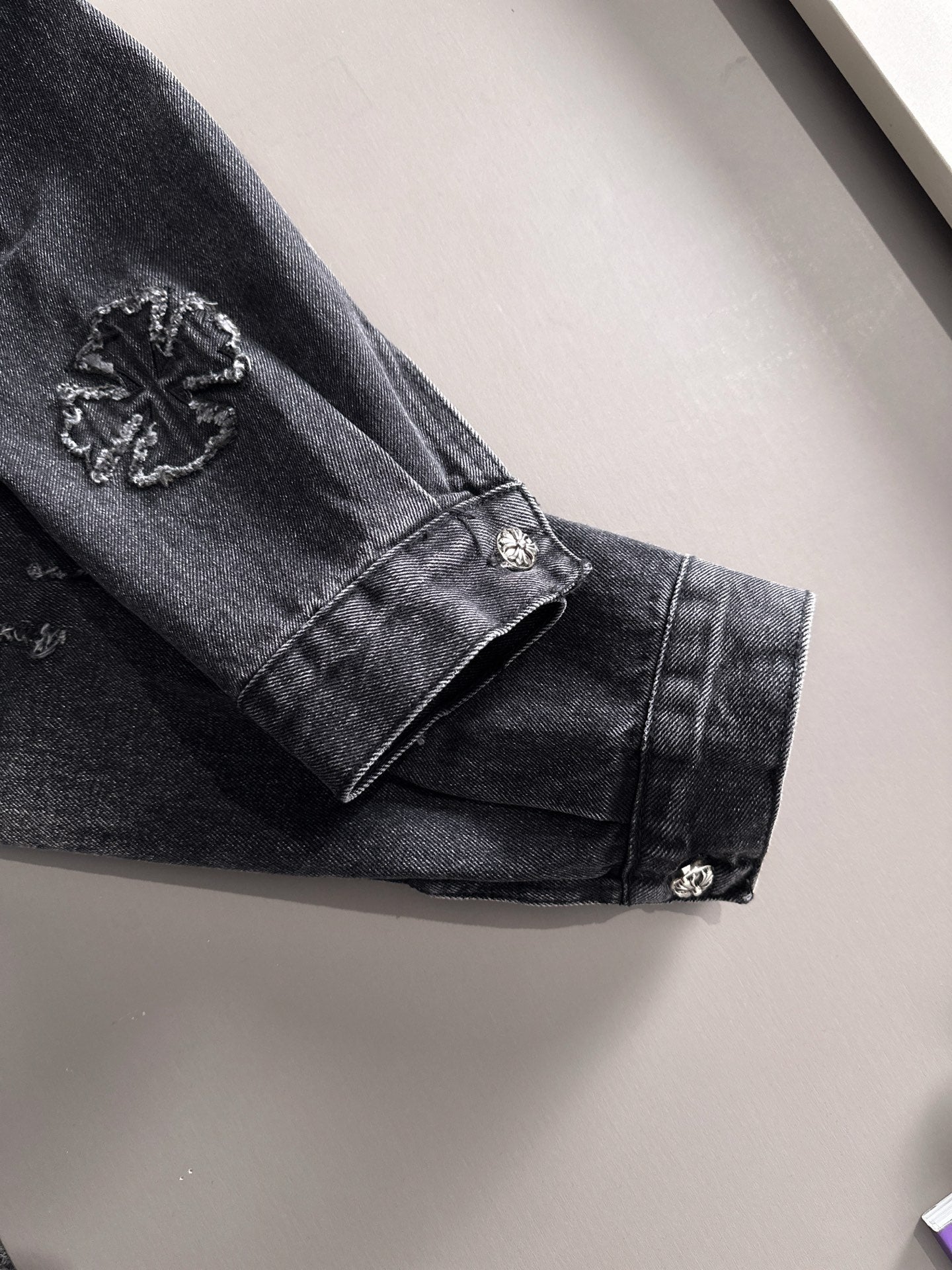 Dark denim jacket sleeve cuff with button and embroidered patch accents