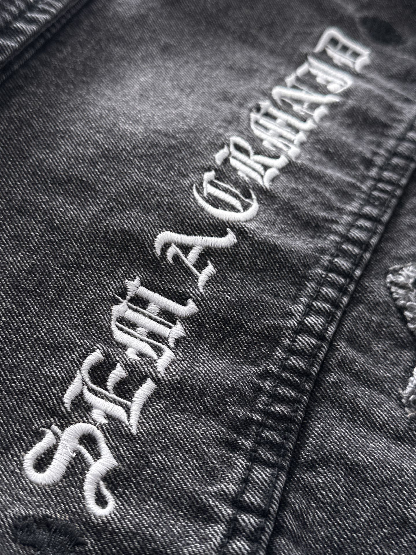 Dark denim jacket graphic embroidery on sleeve cuff with distressed lettering
