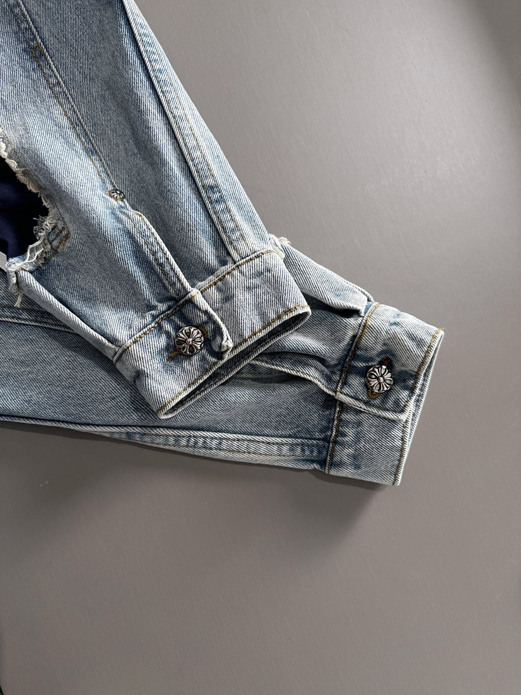 Light blue denim jacket cuff with small metal button and embroidered dark motifs