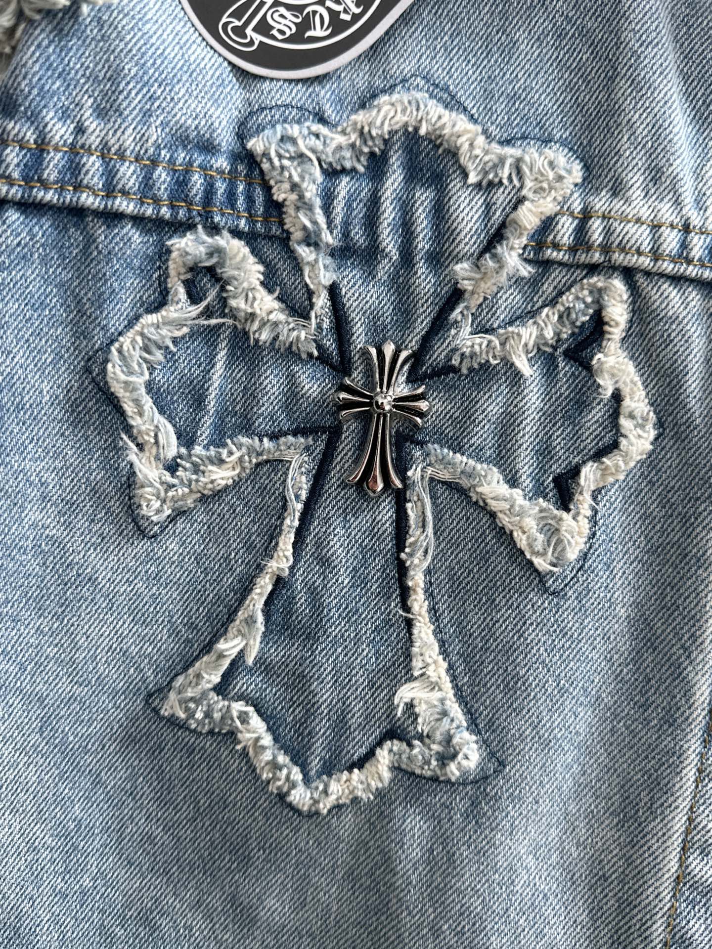 Light blue denim jacket with star-shaped embroidered cross appliqué on chest