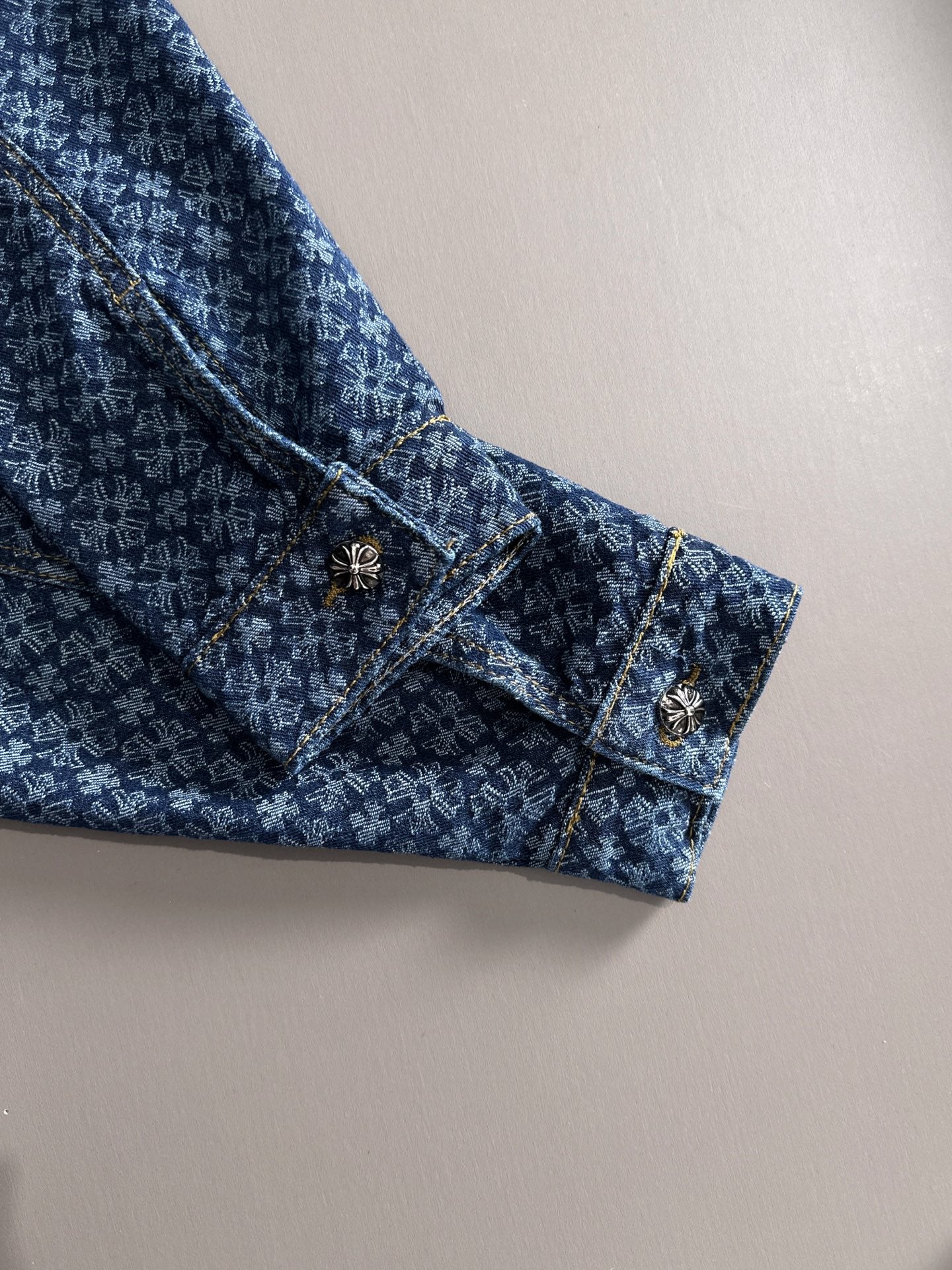 Blue patterned denim jacket sleeve cuff with decorative buttons and gold trim