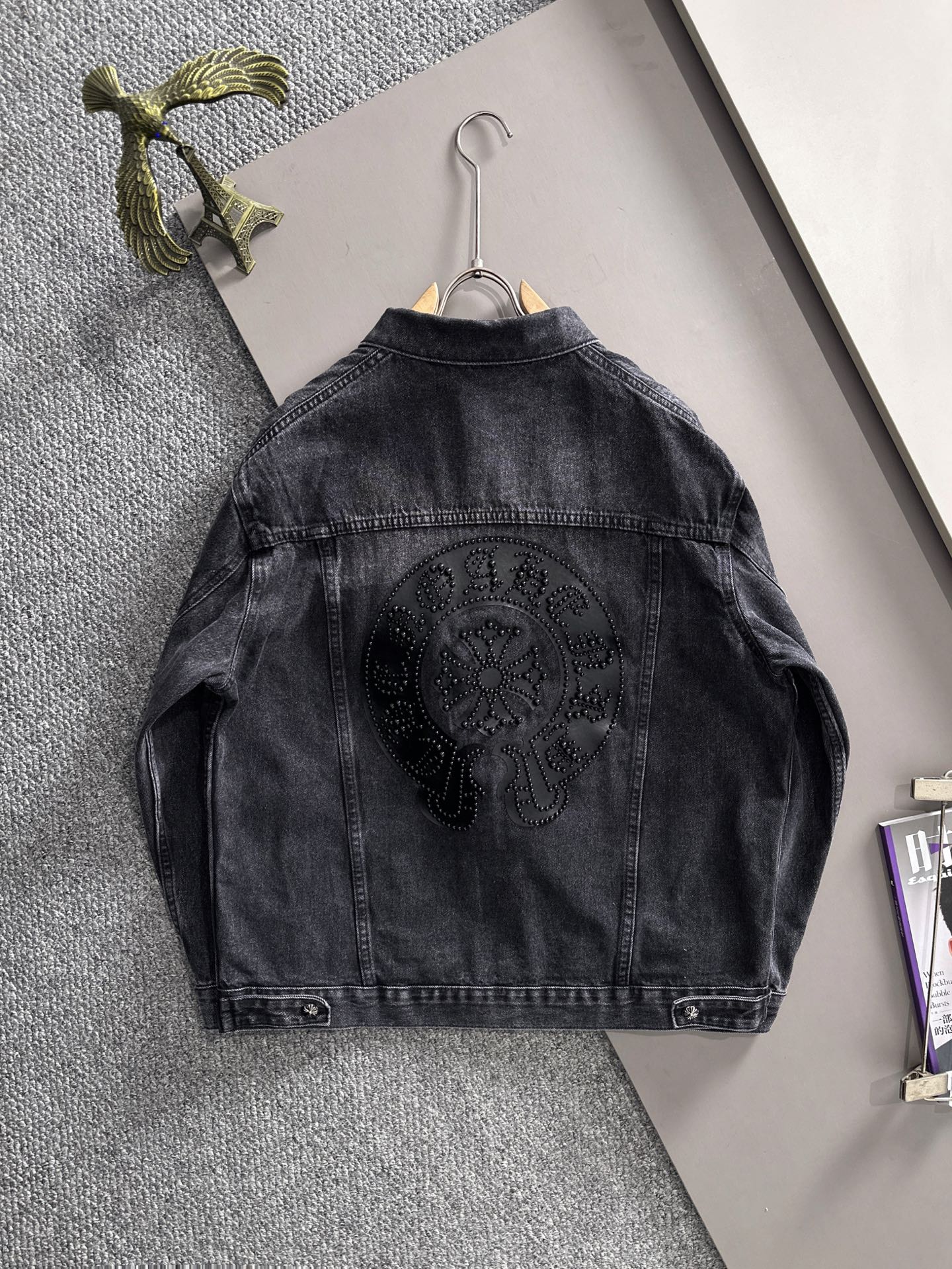 Dark denim jacket back view on hanger with large circular studded emblem